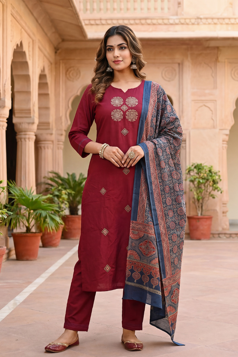Woman in a maroon traditional outfit with a blue patterned dupatta standing in an architectural setting.