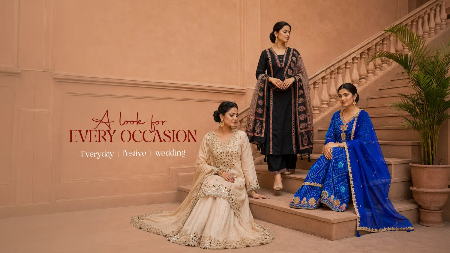 Three women modeling traditional South Asian salwar kameez and suits in an elegant indoor setting with a staircase. The left model wears a cream-colored embroidered gown, the middle model wears a black kurta with gold embroidery, and the right model wears a royal blue salwar suit with gold embroidery.